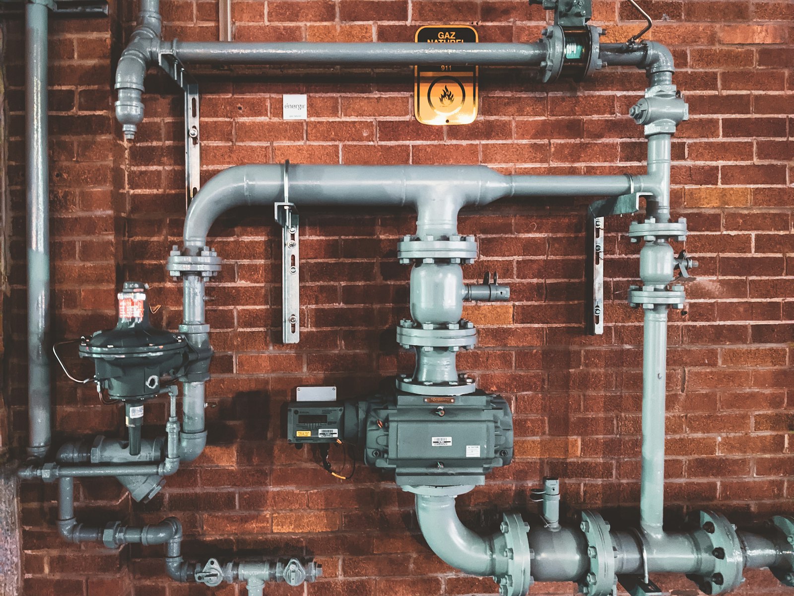 A run of metal plumbing pipes and valves on a brick wall